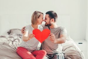 ベッドの上で赤いハートを持つ笑顔の男女