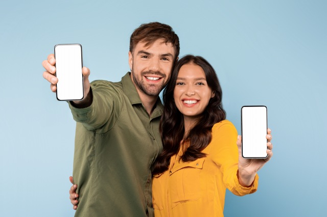 笑顔の若い男女が白い画面のスマートフォンを提示