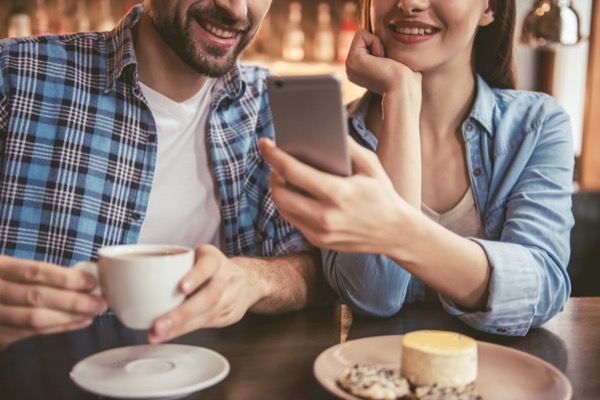 カフェでスマートフォンを見ているカップルの画像