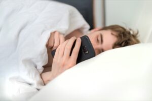 ベッドの中でスマートフォンを操作画像